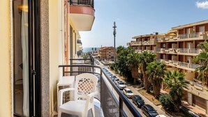 Een balkon met een witte stoel en tafel, met uitzicht op een straat met auto’s en palmbomen.