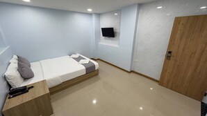 A modern hotel room with a bed, a wooden bedside table, a mounted TV, and a wooden door. - Affordable Single | Central Thailand Stay (Bangkok)