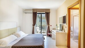 Une chambre d’hôtel avec un lit, un bureau, une chaise et une télévision. Il y a un balcon avec une chaise et une table.