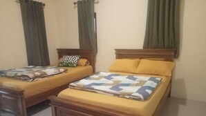 Dos camas de madera con ropa de cama amarilla y mantas estampadas, una mesita de noche de madera y cortinas verdes.