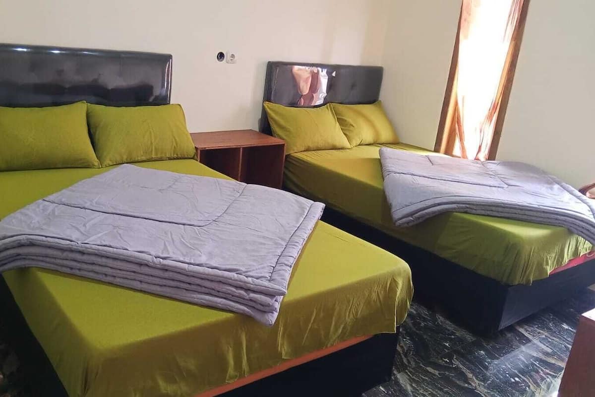 Une chambre d’hôtel avec deux lits, chacun étant agrémenté de draps verts et d’une couverture grise. Une table de chevet en bois se trouve entre les deux lits.