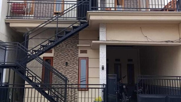 Un edificio residencial de dos pisos con fachada de piedra, una escalera central y un balcón en el piso superior.