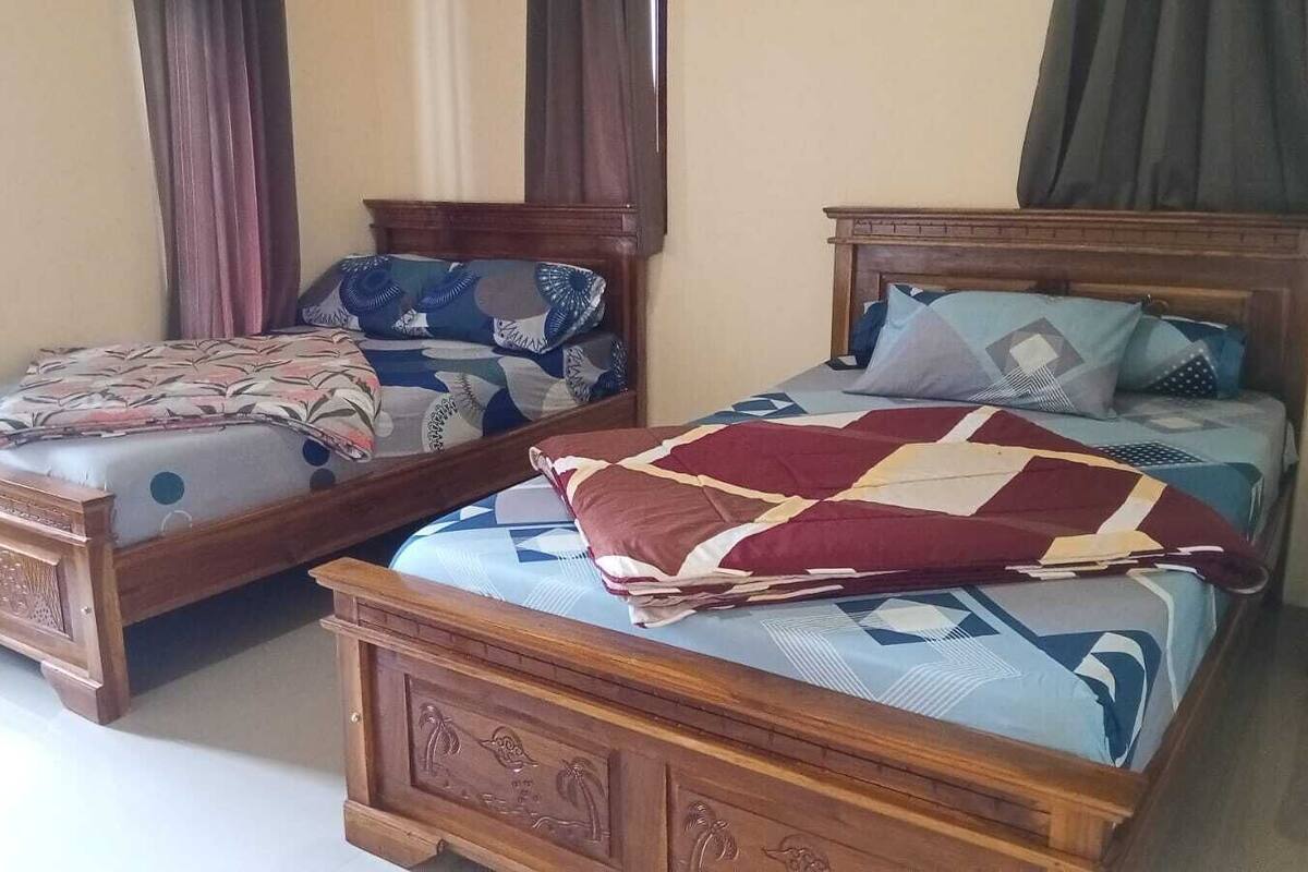 Une chambre avec deux lits en bois, chacun recouvert d’une courtepointe et agrémenté d’oreillers aux motifs différents.