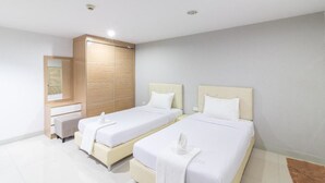 Une chambre d’hôtel moderne avec deux lits simples, une armoire en bois, un petit coin salon et un miroir.