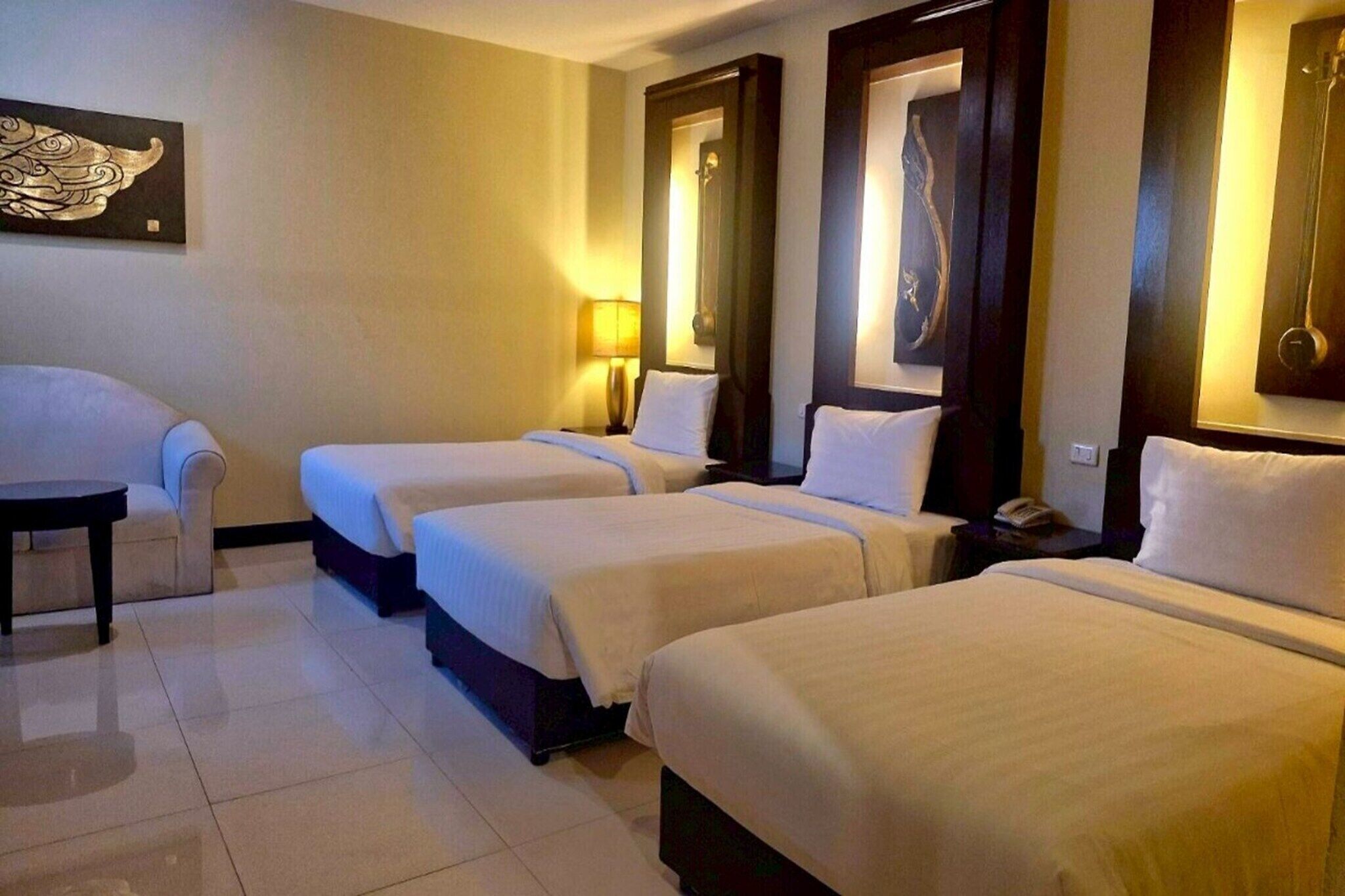 A hotel room with three single beds, a small table, a chair, and a lamp.