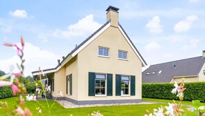 Une maison moderne à deux étages, dotée d’un toit en pente, d’un petit porche à l’avant et d’une pelouse bien entretenue.