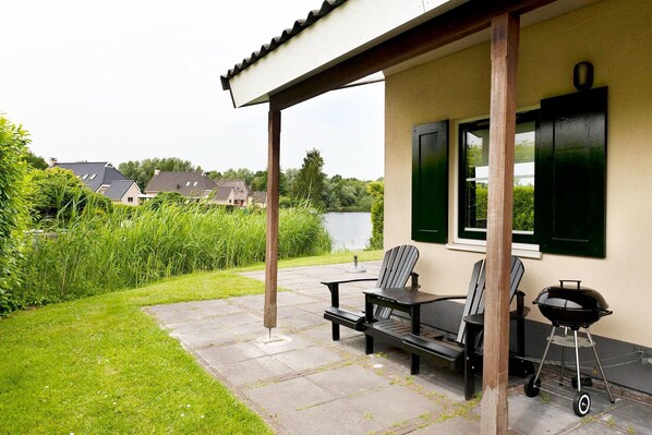 An outdoor patio with a table and chairs, a grill, and a view of a lake and houses in the background.