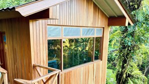 A wooden cabin with a balcony and large windows overlooking a lush garden. - Hilltop Retreat Beneath Mt. Batukaru (Selemadeg)