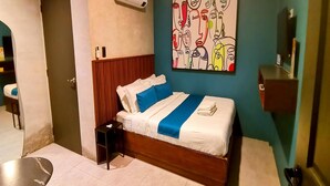 A hotel room with a bed, a nightstand, a wall-mounted air conditioner, and a painting. - Modern Standard Double | Easy Access to Clark (Pampanga)
