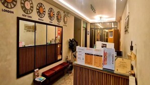 A hotel reception area with clocks displaying times for London, New York, Manila, Dubai, and Tokyo. There is a reception desk with informational brochures and a seating area with a bench. - Smart Solo Stay | Cozy Single Near Clark Airport (Pampanga)