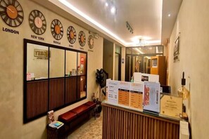 En hotellobby med klockor som visar aktuell tid för London, New York, Manila, Dubai och Tokyo. Det finns en receptionsdisk med informationsbroschyrer och en sittgrupp med en bänk.