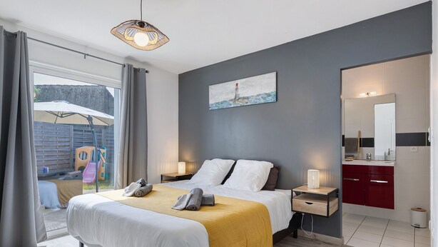 Un dormitorio con cama, mesitas de noche, un espejo, un cuadro y vistas al exterior.