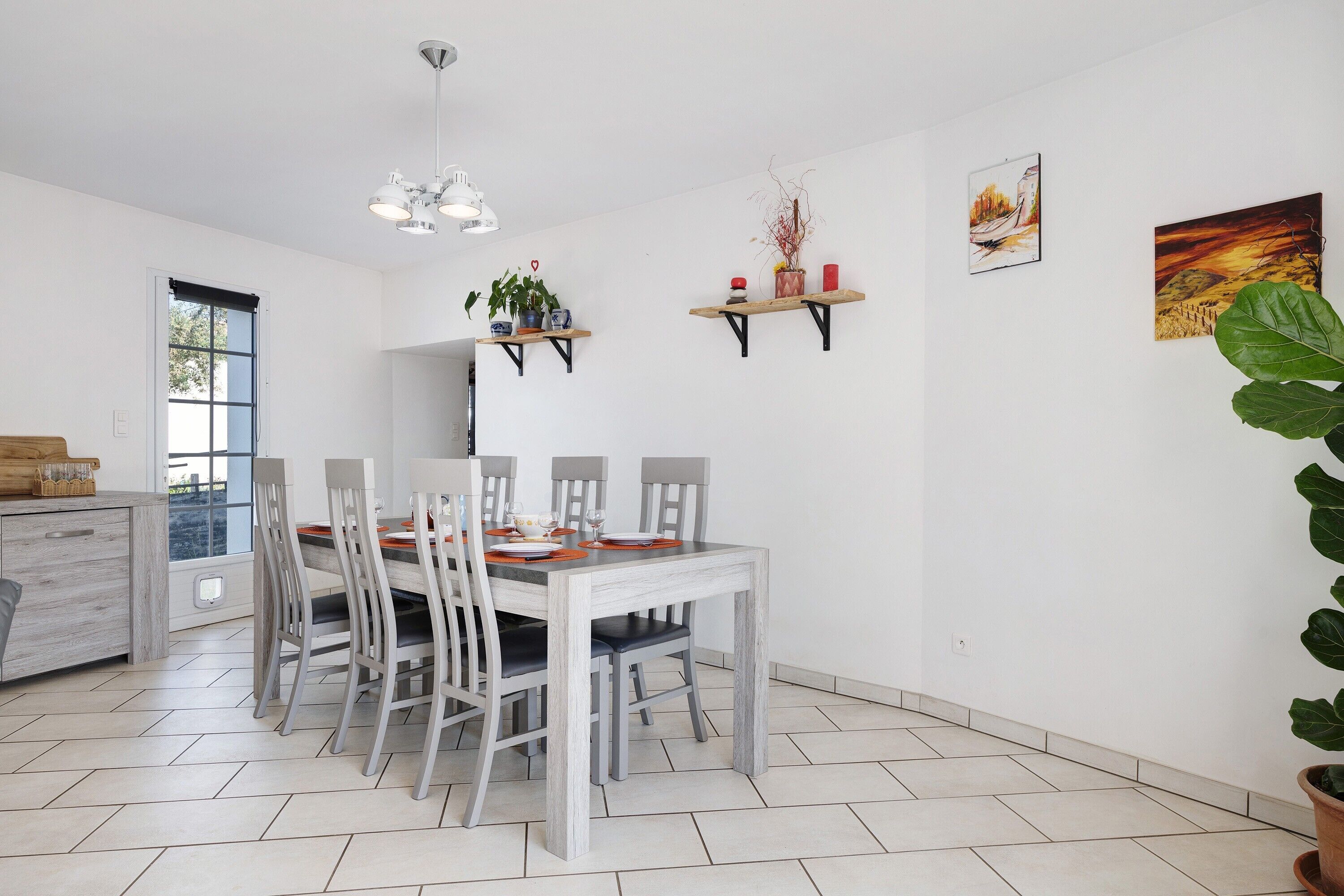 Un coin repas avec une table blanche, des chaises grises, un buffet en bois et une fenêtre.