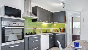 Una cocina moderna equipada con microondas, horno y lavavajillas, una zona de comedor con mesa y sillas, y vistas al exterior.