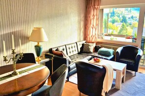 A modern living room with a sofa, chairs, a dining table, and a view of a green landscape through the window. - Haus Sonnenschein an der Skipiste (Herrischried)