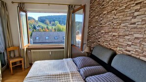 A bedroom with a large bed, a view of a house through a window, a stone wall, and a wooden chair. - Haus Sonnenschein an der Skipiste (Herrischried)
