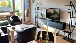 A modern living room with a TV, comfortable seating, a small table, and a view of the outdoors. - Haus Sonnenschein an der Skipiste (Herrischried)