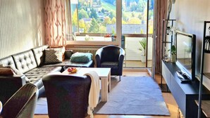 A living room with a sofa, armchairs, a coffee table, and a TV. There is a large window with a view of a green landscape. - Haus Sonnenschein an der Skipiste (Herrischried)