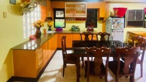 A kitchen with a dining table and chairs, a refrigerator, and a window with curtains.