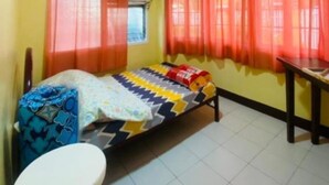 Una habitación pequeña con una cama individual, una colcha colorida, un escritorio de madera y una ventana con cortinas naranjas.