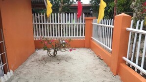 Un patio con cerca blanca de piquetes, paredes anaranjadas y una planta pequeña con flores rosas.