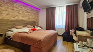 Quarto de hotel moderno com uma cama grande, uma escrivaninha, uma cadeira e uma televisão.