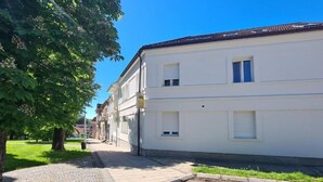 Um edifício branco com telhado ladrilhado, calçada pavimentada e rua arborizada.