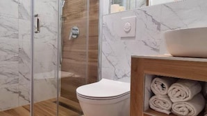 Un baño moderno con cabina de ducha de vidrio, inodoro y tocador con lavabo y toallas.