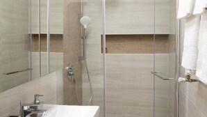 Ein modernes Badezimmer mit einer Duschkabine aus Glas, einem weißen Waschbecken und einem Handtuch an der Wand.
