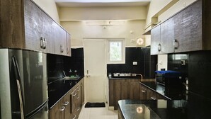 Une cuisine avec des meubles de rangement en bois foncé, un réfrigérateur en acier inoxydable et un plan de travail noir.