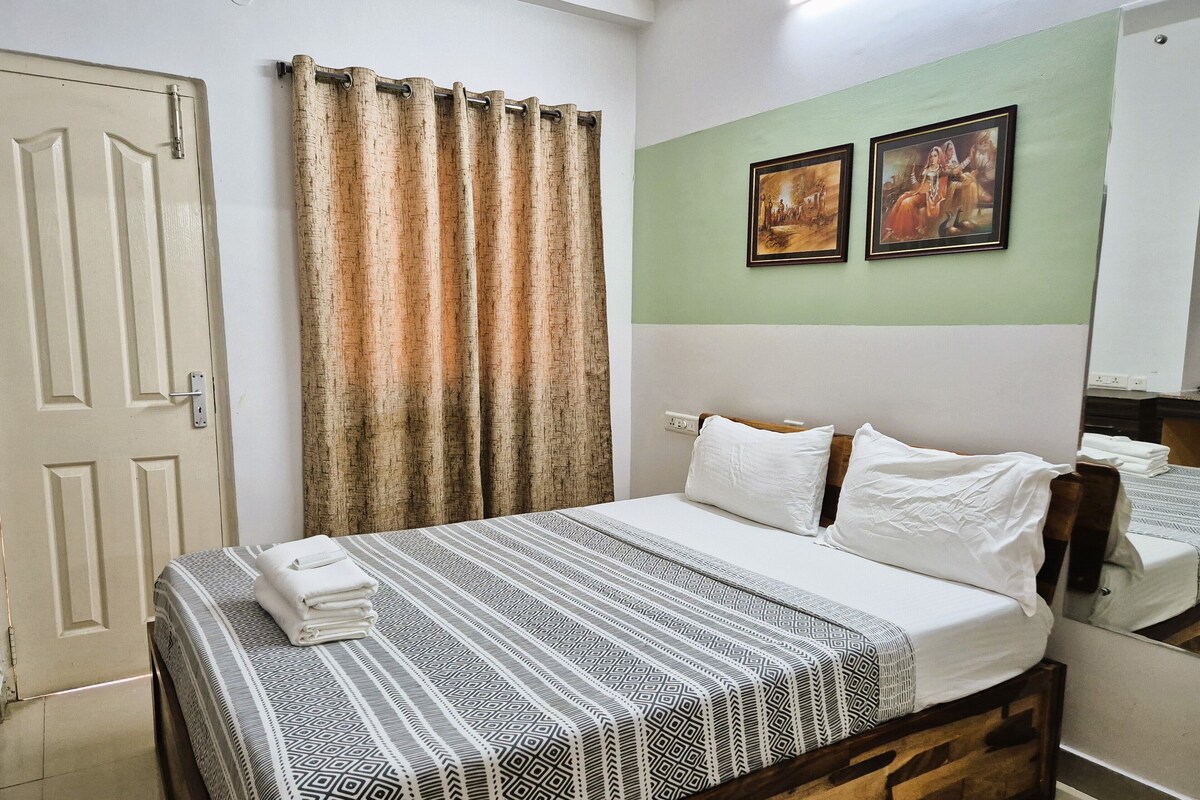 Une chambre à coucher avec un lit, des rideaux, un mur orné de deux tableaux encadrés et une porte.