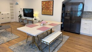 A modern kitchen with a refrigerator, a dining table with benches, a TV, and a painting on the wall. - 1940’s Beauty near downtown, medical center and UH (Houston)