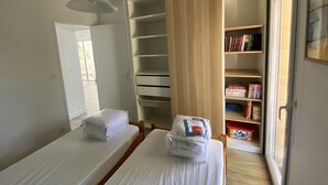 Quarto com duas camas, um guarda-roupa de madeira e uma estante repleta de livros.