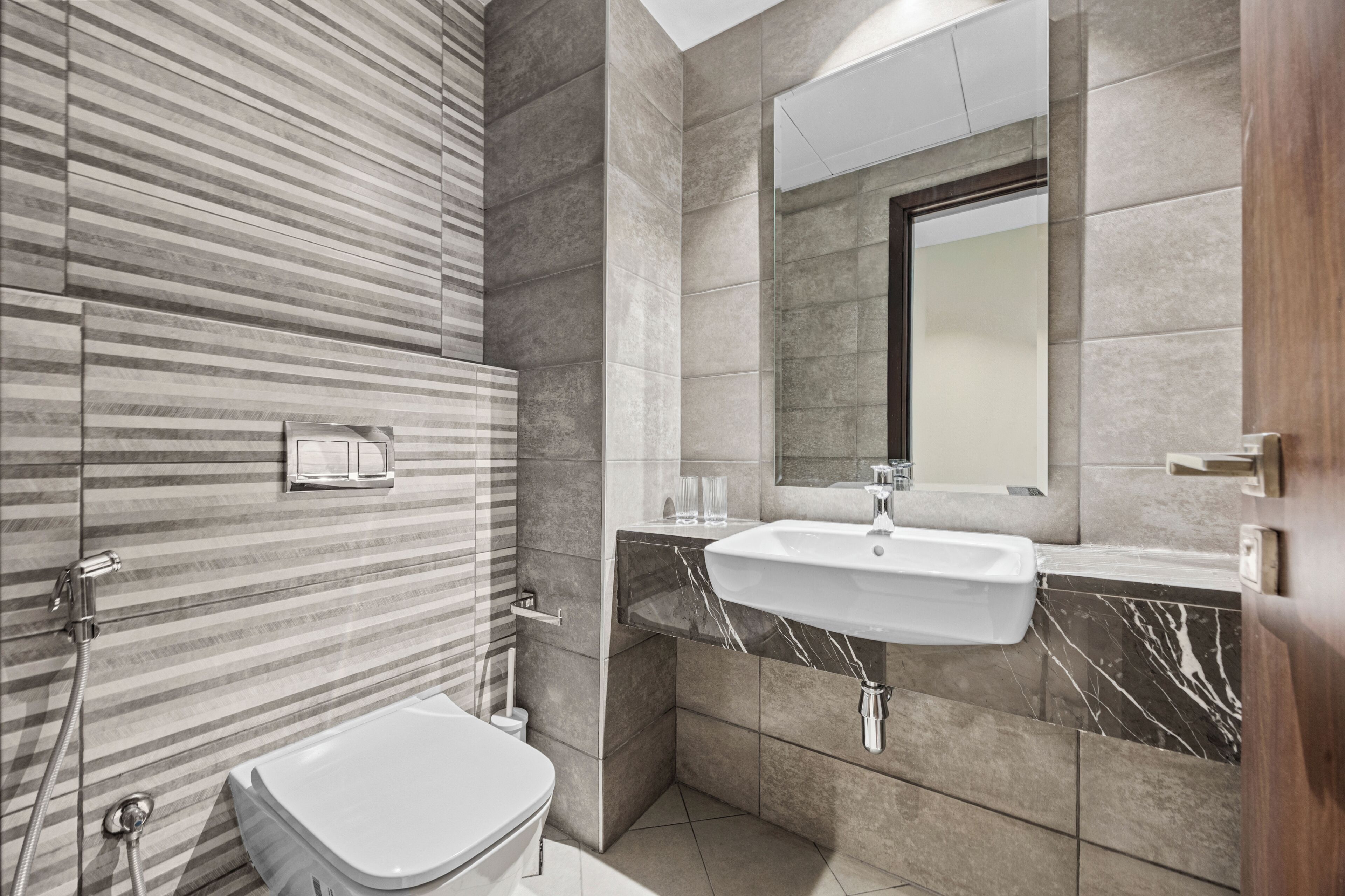 Een moderne badkamer met een gestreepte wand, een wit toilet, een wastafel met een marmeren aanrechtblad en een spiegel.