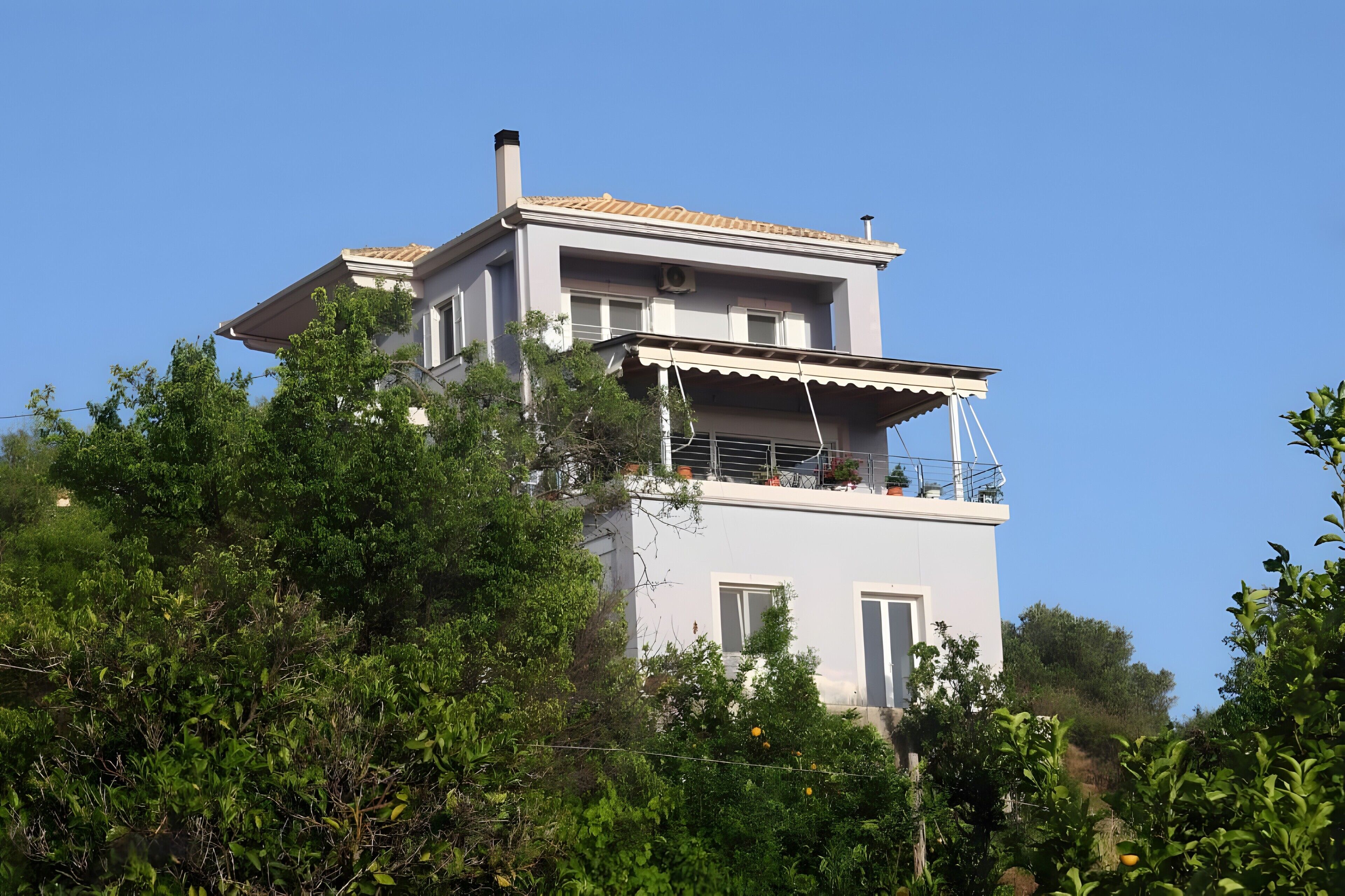 Edificio de dos pisos con balcón, rodeado de vegetación.