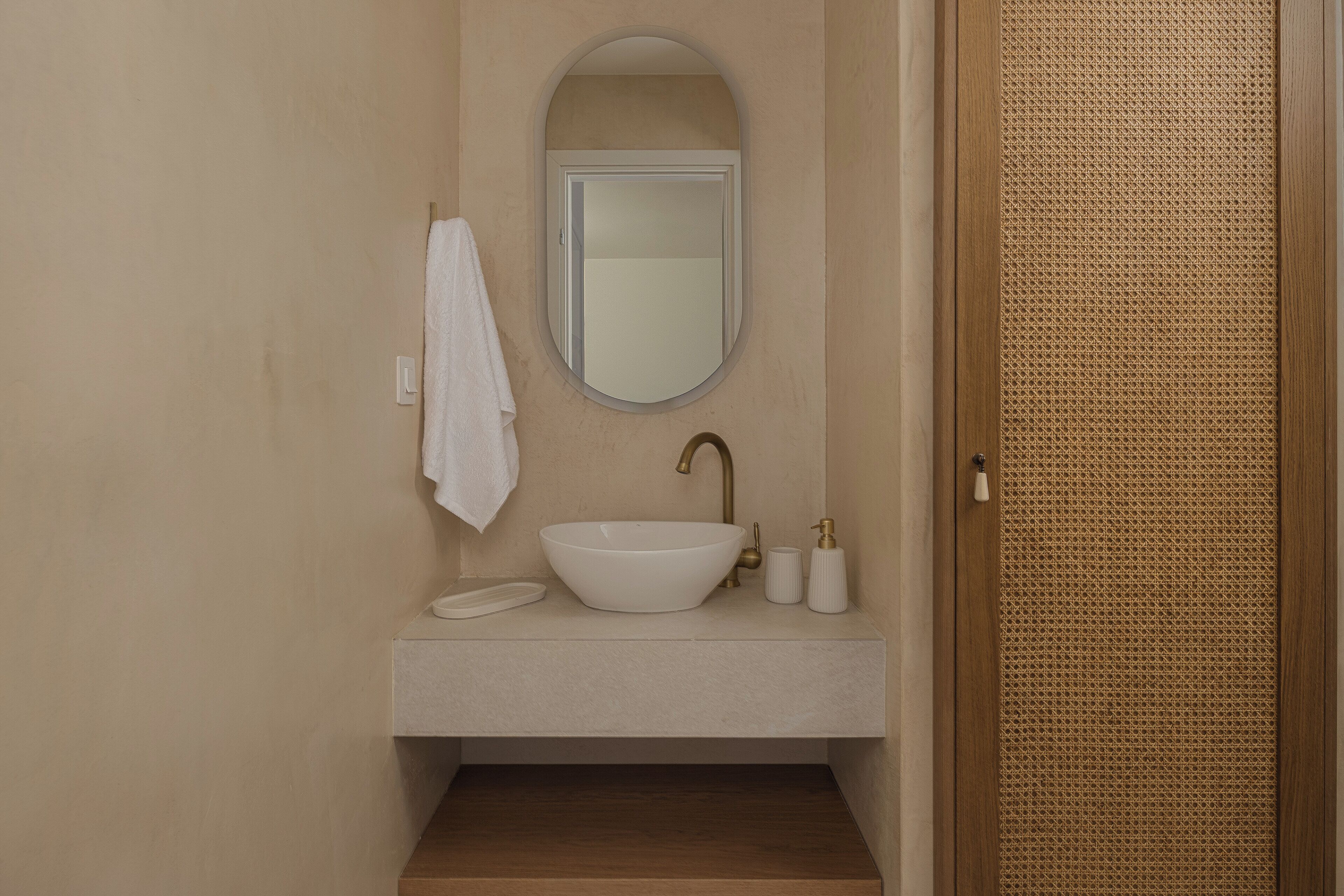 Een badkamer met een witte wastafel, een spiegel en een handdoek aan de muur.
