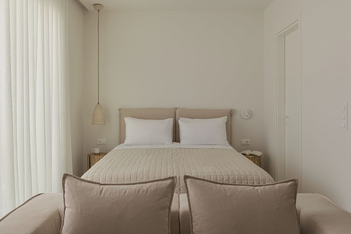 Une chambre à coucher avec un lit, des tables de chevet, un luminaire suspendu et une porte.