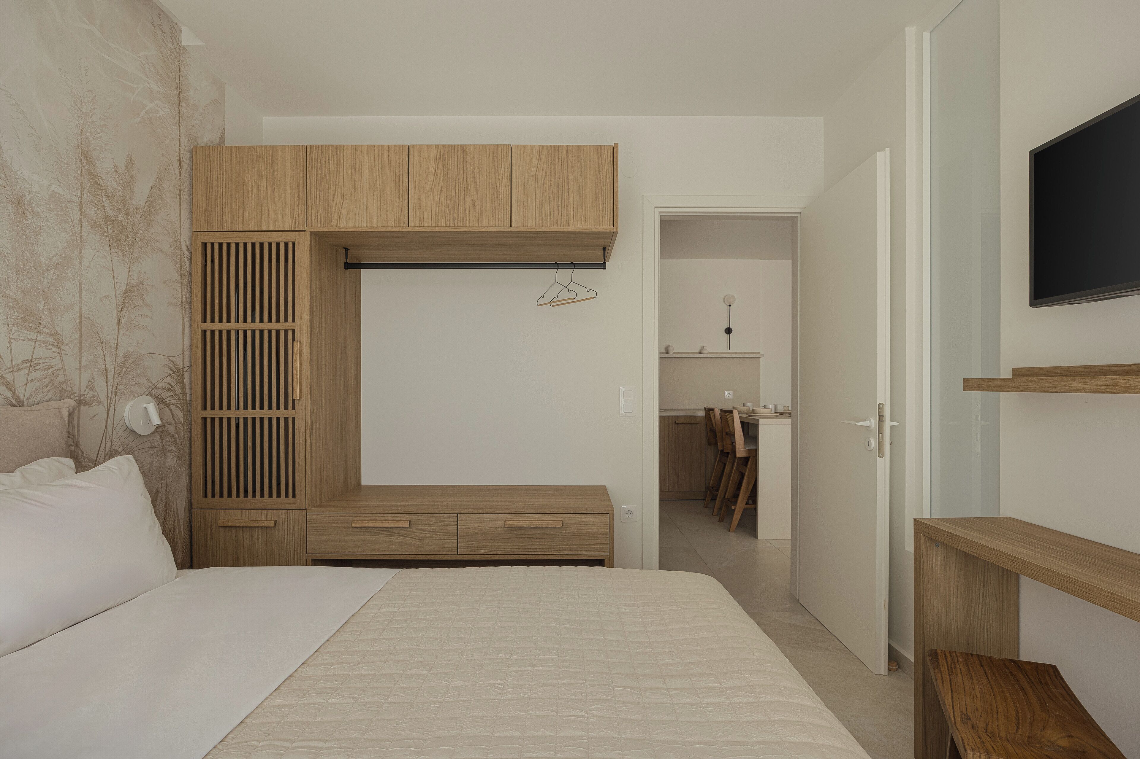 A bedroom with a bed, wooden wardrobe, and a TV on the wall.