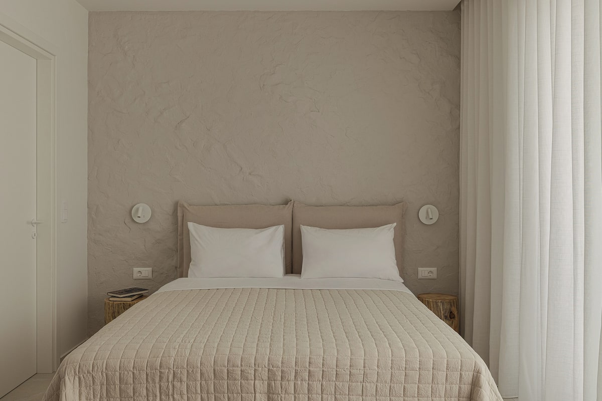 Une chambre à coucher comprenant un lit, deux tables de chevet et un luminaire fixé au mur.
