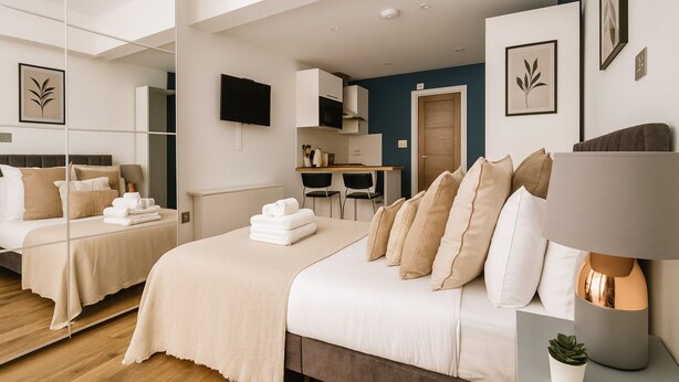 A modern hotel room with a large bed, a desk, a chair, a TV, and a mirror. - Modern Studio Flat in Hammersmith (London)