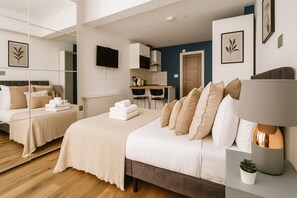 A modern hotel room with a large bed, a desk, a chair, a TV, and a mirror. - Modern Studio Flat in Hammersmith (London)