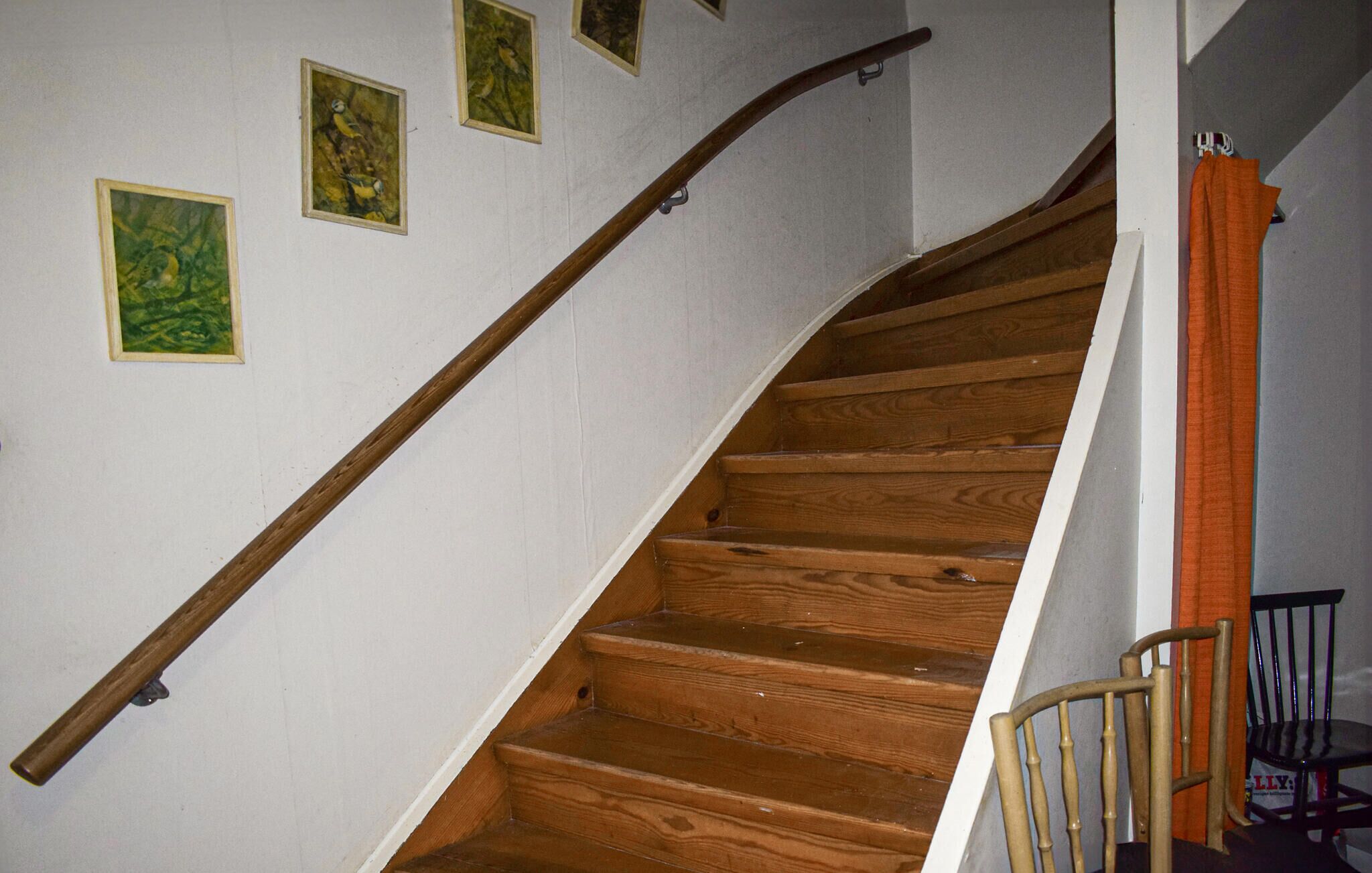 A wooden staircase with a handrail, wooden steps, and a white wall with framed pictures.