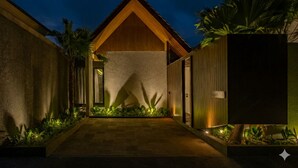 A modern building with a wooden facade, a concrete pathway, and tropical plants. - Modern 3bedroom villa with calm surrounding (Kabupaten Gianyar, Bali)