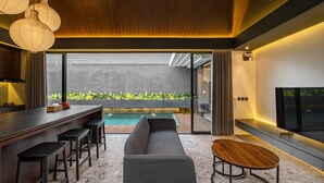 A modern kitchen with a bar area, a gray sofa, and a wooden table. - Modern 3bedroom villa with calm surrounding (Kabupaten Gianyar, Bali)
