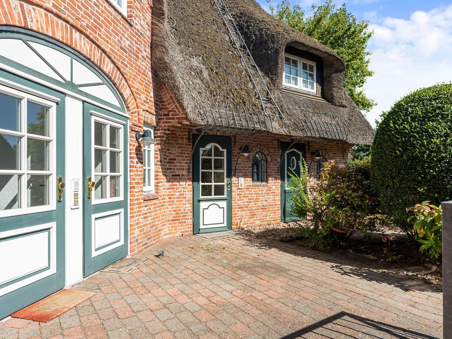 A traditional brick house with a thatched roof, a large arched window, and a door with a green frame.