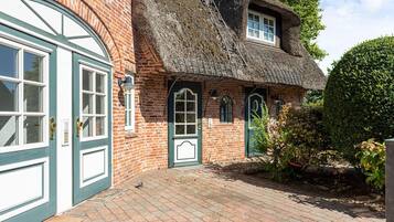 A traditional brick house with a thatched roof, a large arched window, and a door with a green frame.