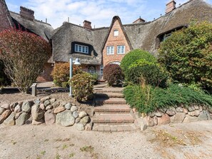 A traditional thatched-roof house with a brick extension, stone steps, and a stone wall. - Altstadttor 17 - Thatched-roof vacation apartment for up to two people (Sylt)