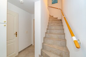 Een trap met een leuning, een deur met een gouden handvat en een lichtschakelaar aan de muur.