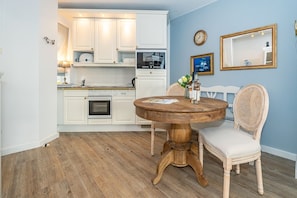 A modern kitchen with white cabinets, a wooden dining table, and a round mirror. - Altstadttor 17 - Holiday apartment under thatch for up to two people in (Sylt)