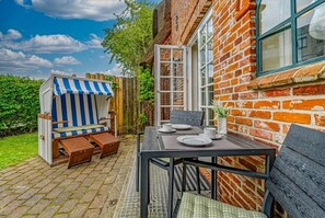 A patio with a striped beach chair, a table set for two, and a brick wall. - Altstadttor 17 - Holiday apartment under thatch for up to two people in (Sylt)